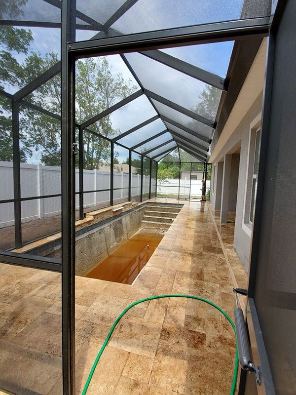 Covered outdoor walkway with black metal frame, glass roof, and wet tiled floor beside a pool.
