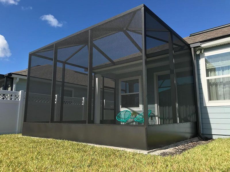 Screened-in patio enclosure attached to a house, with a teal bike inside and grass in front.
