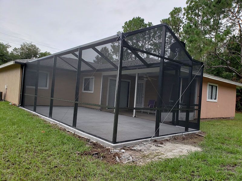 Screened-in backyard patio attached to a tan house, with black mesh framing and a concrete floor