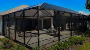 Screened patio enclosure with black frame and mesh over a concrete patio in a sunny backyard