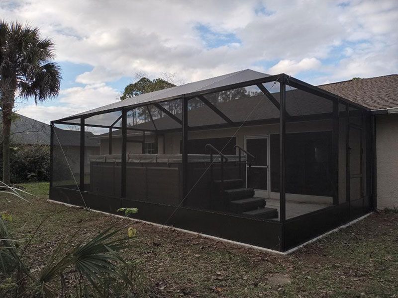 Screened patio enclosure with black frame attached to a house in a backyard