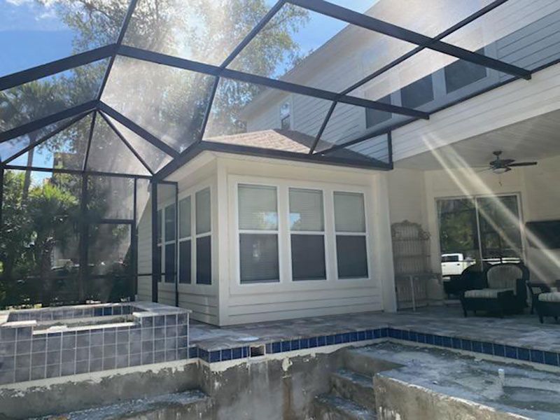 Screened backyard patio with a hot tub, tiled pool, and covered seating area beside a house.