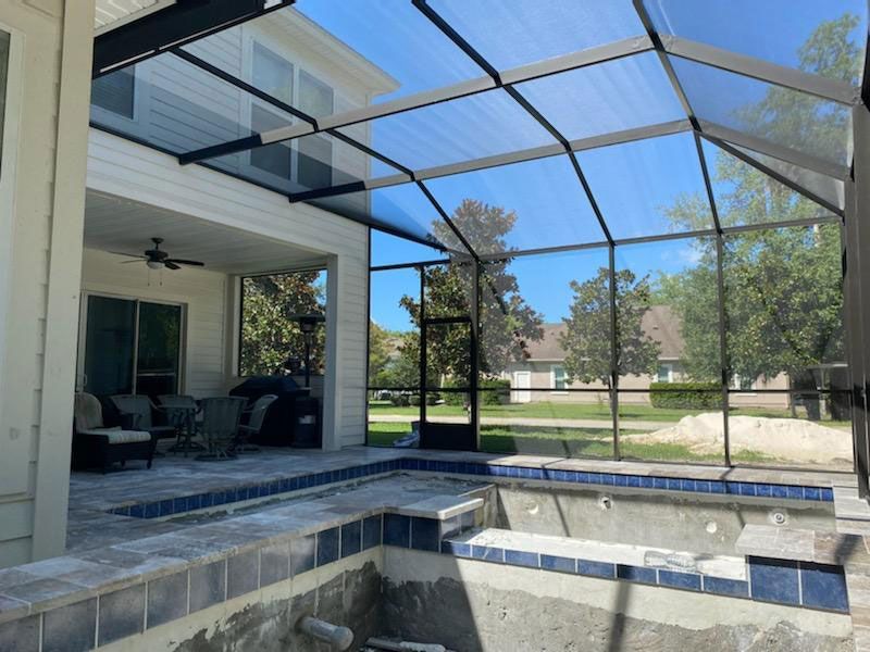Screened patio and empty pool deck with blue water, tile steps, and a backyard view