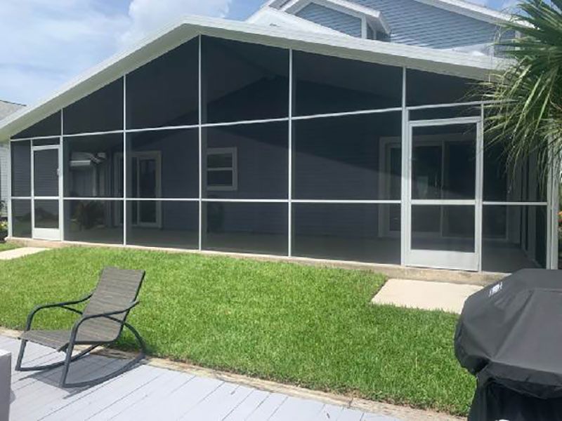 Screened patio and pool enclosure beside a house, with green lawn and two chairs in the foreground.