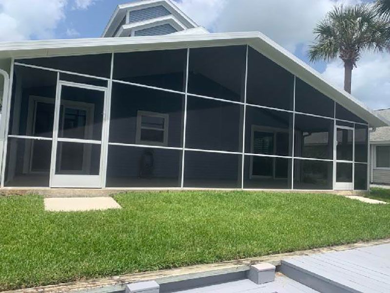 Black screened porch on a house with a white door, green lawn, and palm tree by a sidewalk.