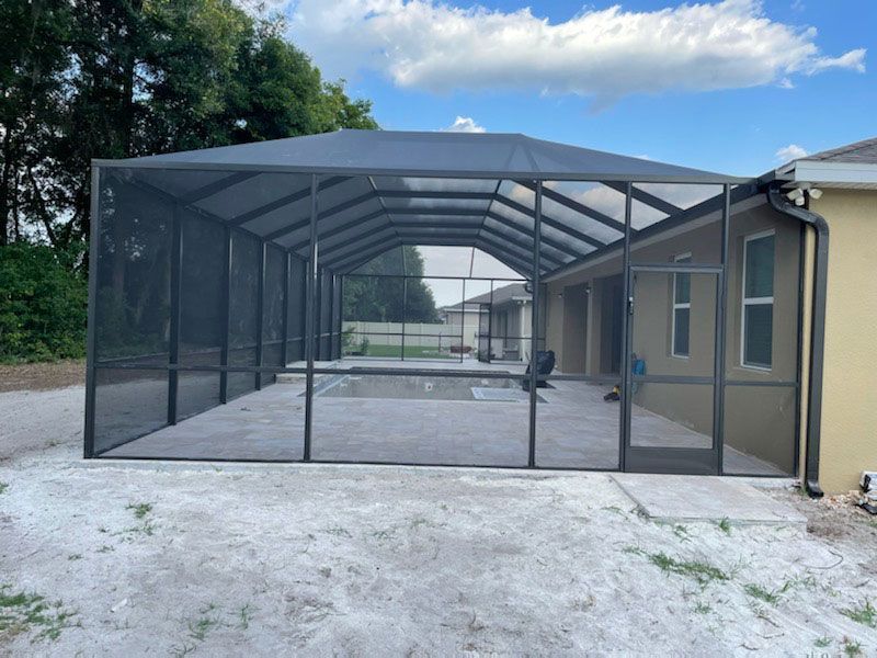 Screened-in backyard patio enclosure with dark frame beside a beige house