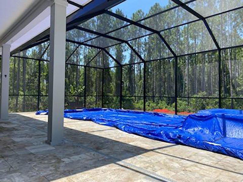 Screened patio with black mesh enclosure, stone floor, and blue tarp covering the ground.