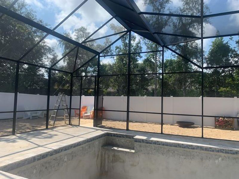 Empty screened-in pool area with unfinished concrete pool and a black metal enclosure under a bright sky