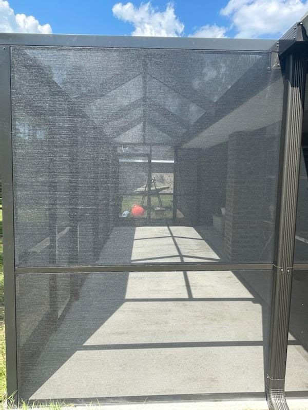 Black mesh kennel corridor with concrete floor and a red ball at the far end under a blue sky