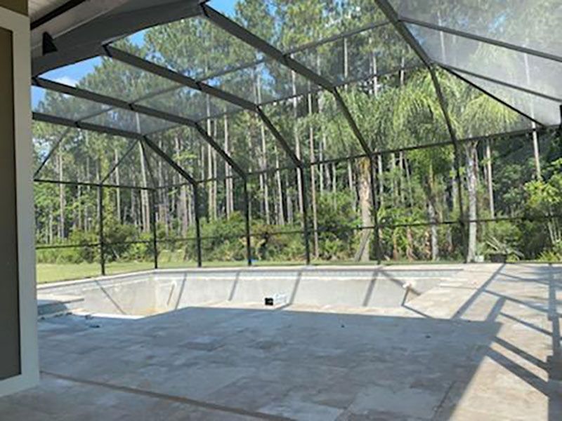 Empty screened-in pool with concrete deck and black frame, surrounded by trees.