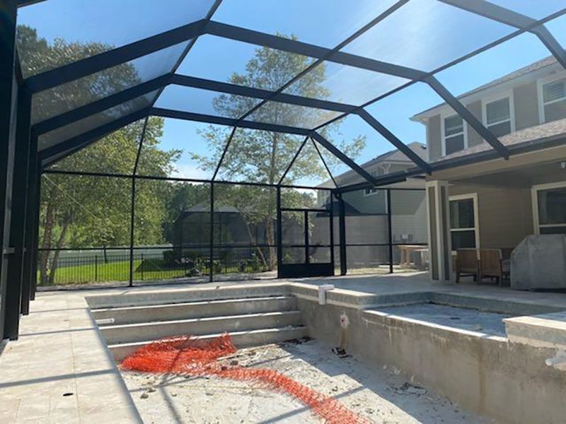 Screened-in backyard patio with concrete steps, poolside ledge, and orange mesh barrier debris