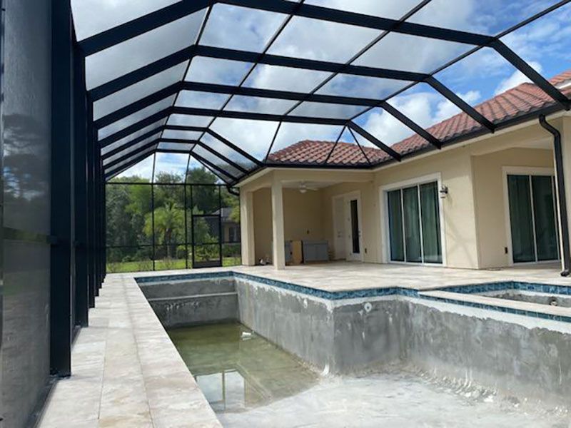 Covered backyard patio with screened pool, white columns, and sliding glass doors under a red-tile roof