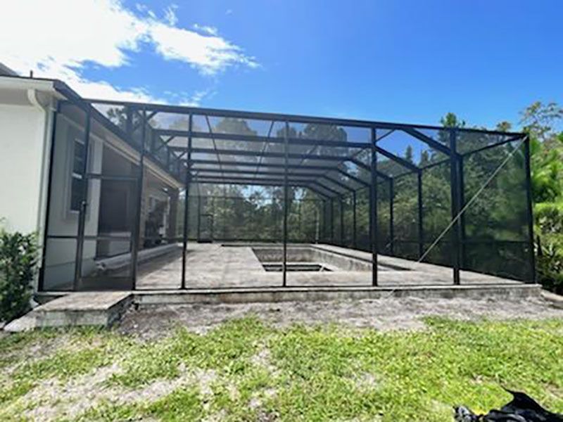 Screened patio enclosure beside a house with concrete floor and steps, under a blue sky