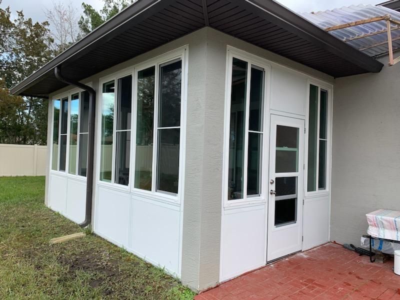White enclosed porch with large windows and a door attached to a house, under construction.