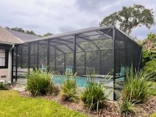 Screened-in backyard pool enclosure beside a house, with landscaping and trees nearby.