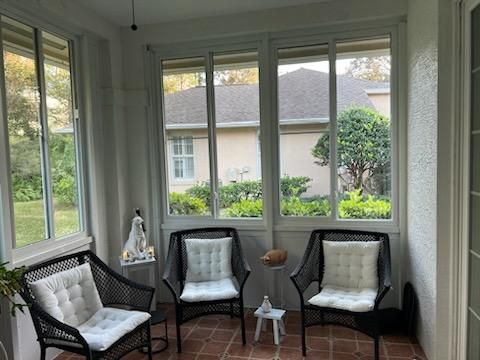 Sunroom with black wicker chairs, white cushions, and large windows overlooking a garden