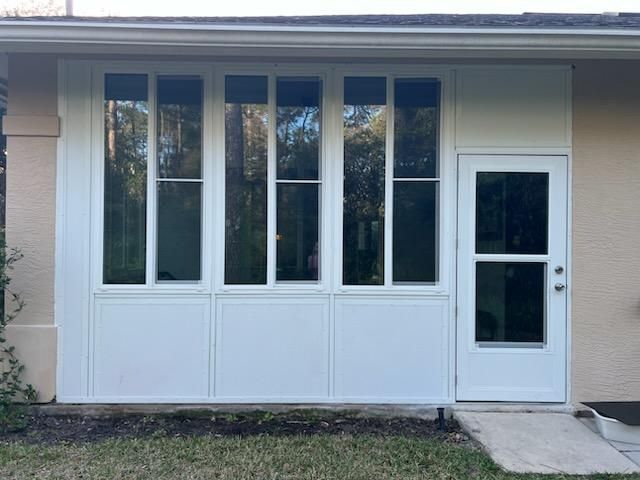 Front porch with white-framed windows and a white side door on a beige house