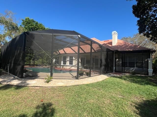 Backyard screened pool enclosure beside a house with red roof under a clear blue sky