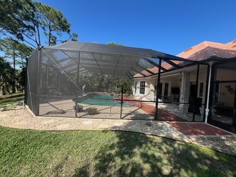 Screened-in backyard pool beside a house, with a covered patio and lawn in the foreground.