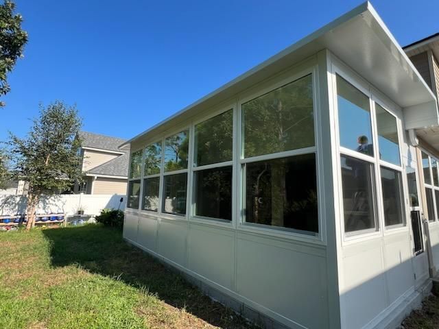 White sunroom addition with large windows beside a grassy yard under a blue sky