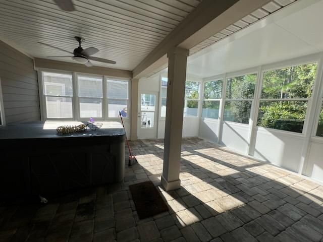 Screened porch with tiled floor, ceiling fan, windows, and sunlight streaming through.