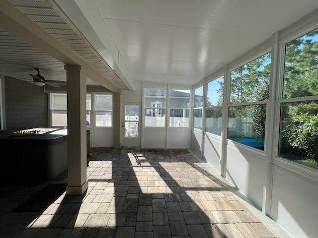 Enclosed sunroom with large windows, white columns, and tiled floor casting bright sunlight shadows.