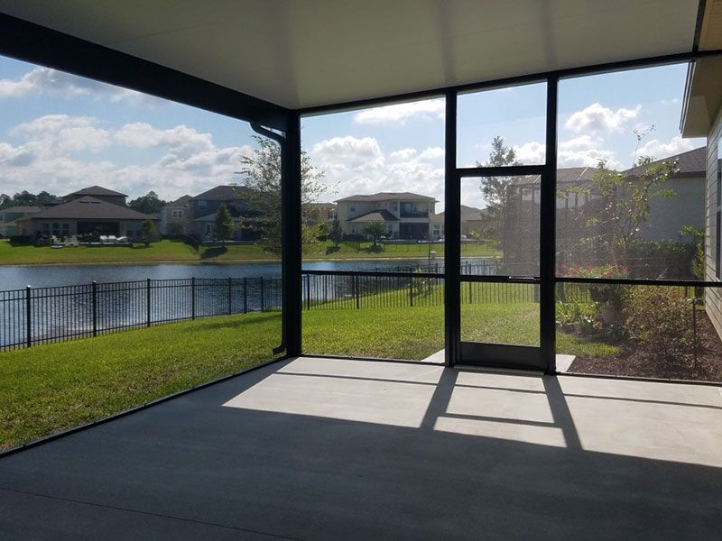Covered patio overlooking a lake and grassy yard, with glass doors and bright sunlight