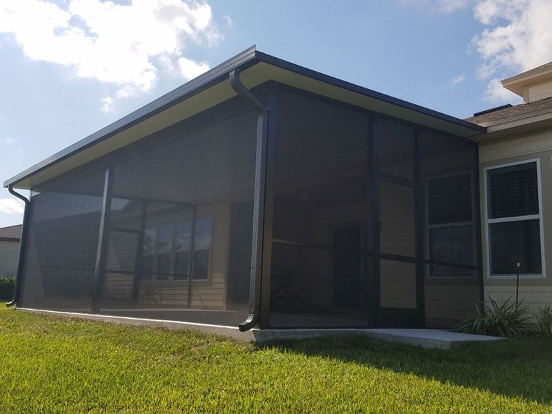 Screened patio enclosure attached to a beige house on a sunny lawn