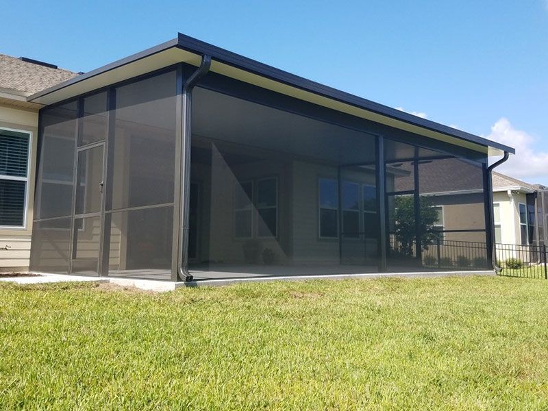 Screened back patio attached to a suburban house with a grassy yard and blue sky