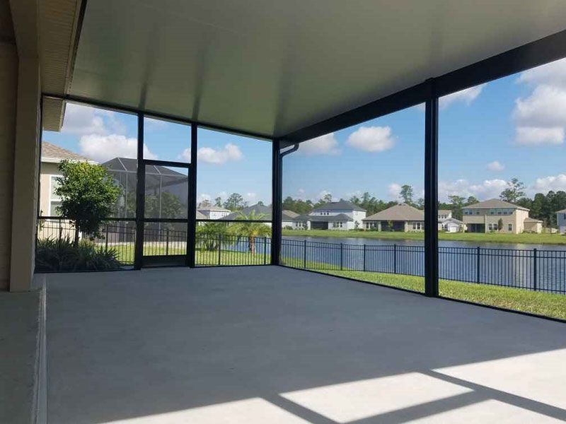 Covered patio with screened enclosure, concrete floor, and view of a lake and houses beyond
