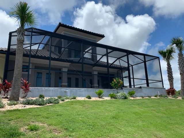 Modern two-story house with a screened porch, white walls, black frame, and green lawn under a cloudy sky