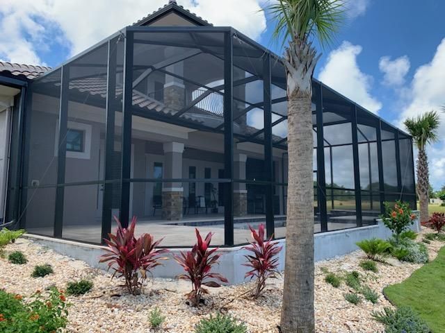 Screened patio enclosure on a modern house, with palm trees and landscaped yard under a blue sky