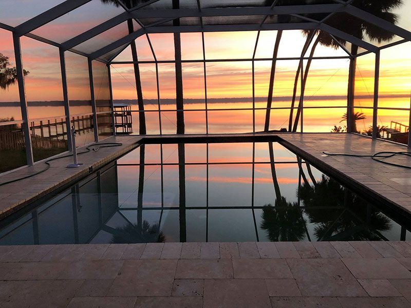 Covered pool at sunset with orange sky reflected in still water and a view of the ocean beyond
