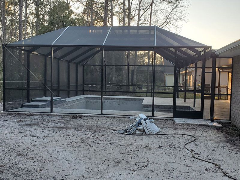 Black mesh screened pool enclosure over an unfinished concrete pool area at dusk