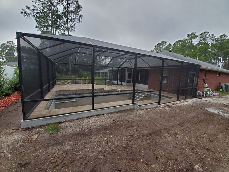 Screened-in patio addition beside a brick house with concrete foundation and dirt yard