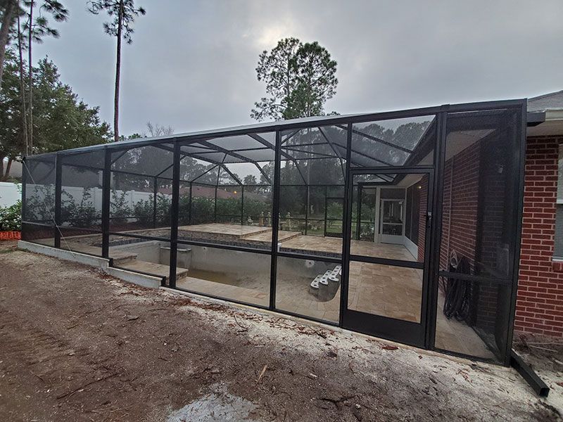 Black mesh enclosure around a concrete patio beside a brick building and dirt yard.