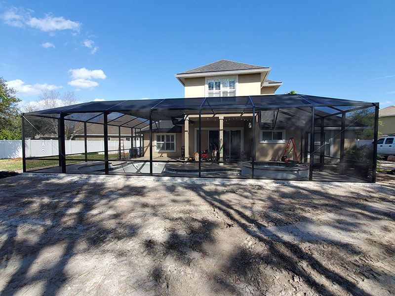 Covered outdoor patio with black metal frame beside a two-story house under a clear blue sky