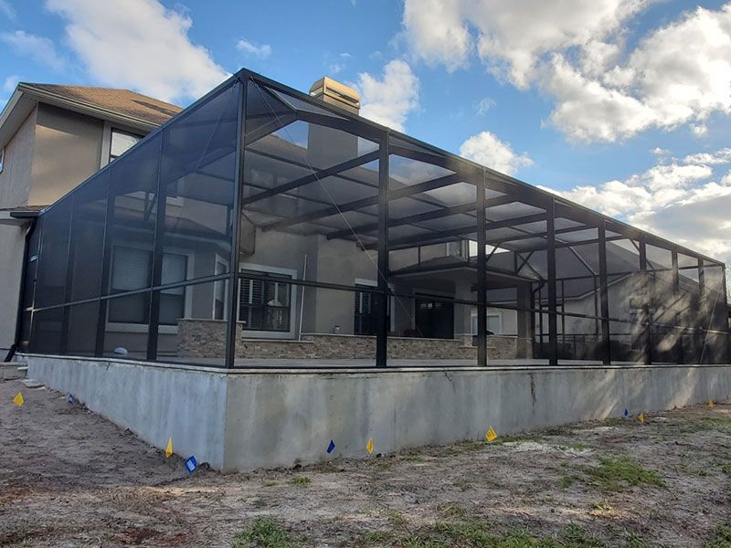 Modern building with a dark mesh screened enclosure over a concrete foundation under a cloudy sky