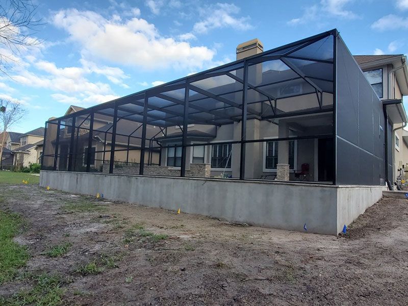 Modern screened-in patio enclosure attached to a concrete house under a blue sky