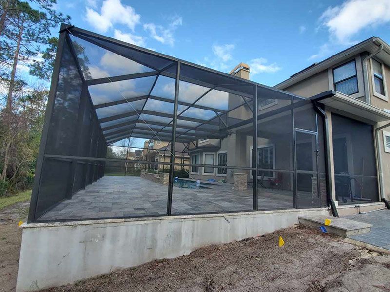 Screened patio enclosure on a concrete deck beside a house under a blue sky