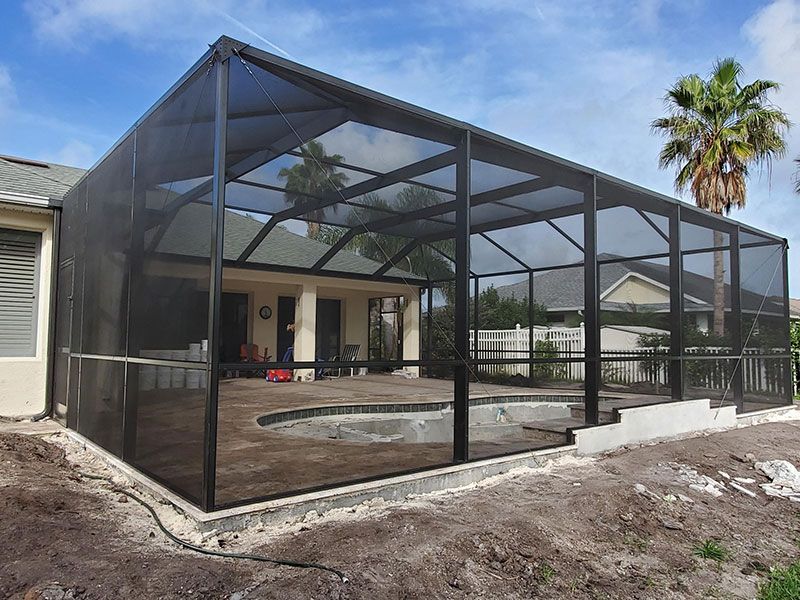 Screened backyard patio with black mesh enclosure, concrete slab, and a house under construction