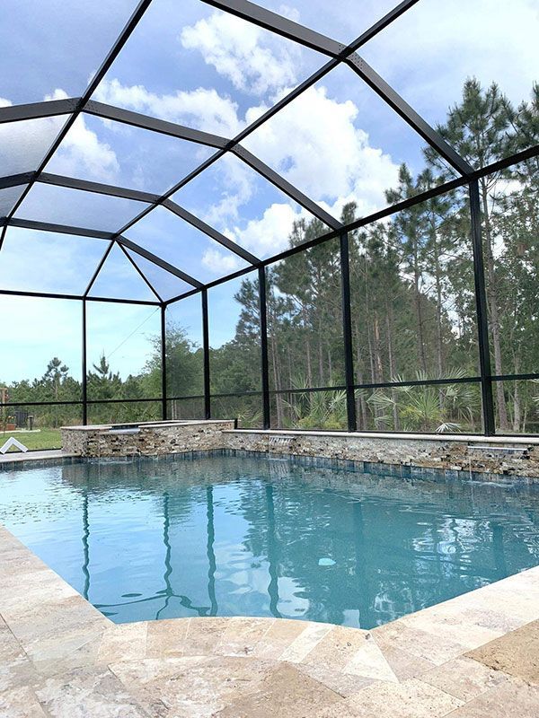 Screened outdoor swimming pool with clear blue water and stone deck under a mesh enclosure