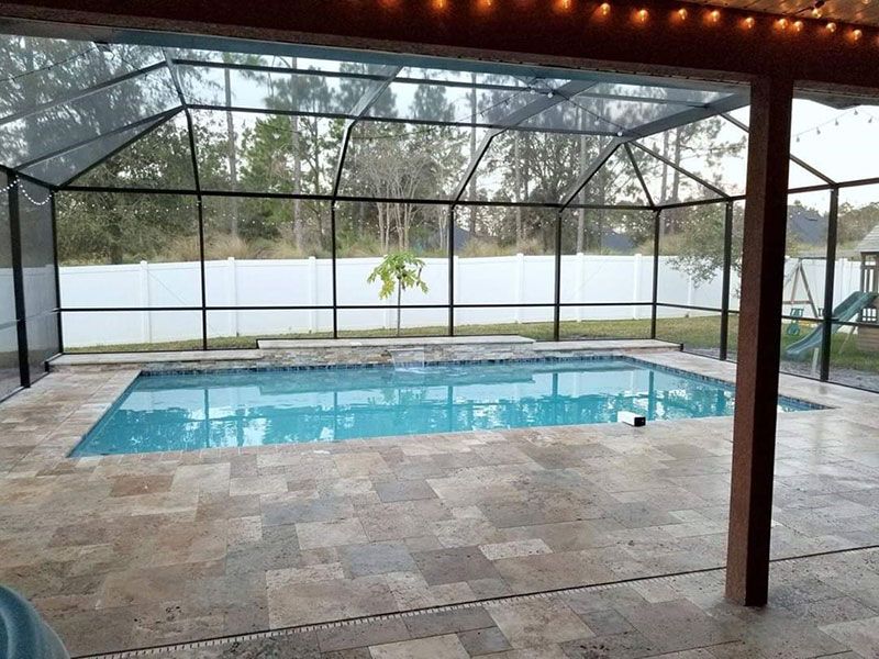 Covered backyard pool with screened enclosure and stone patio, viewed through a shaded patio area