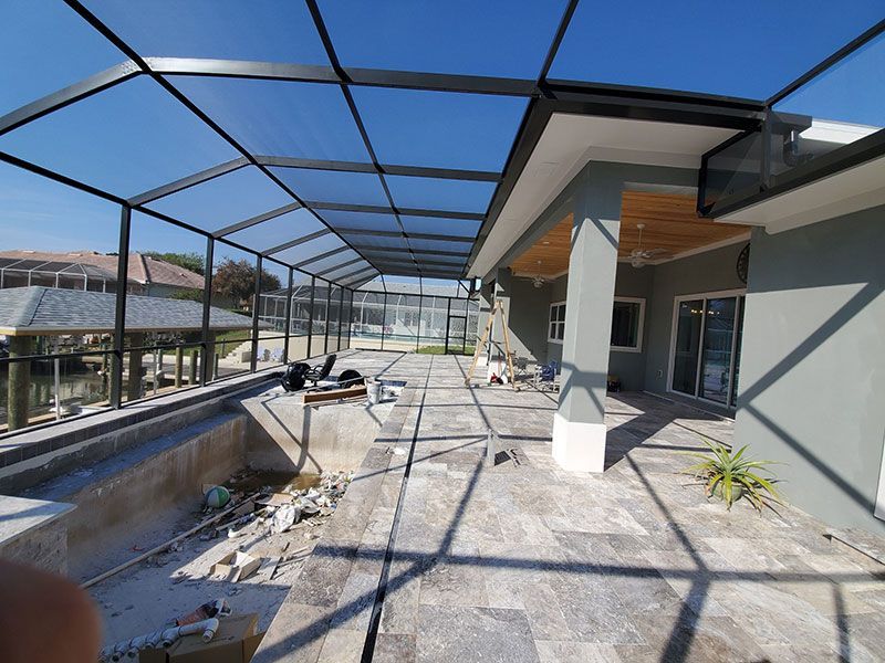 Outdoor patio under a blue net canopy beside a modern house, with potted plants and construction debris