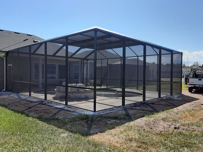 Screened outdoor patio enclosure beside a house, with black frame and mesh panels.