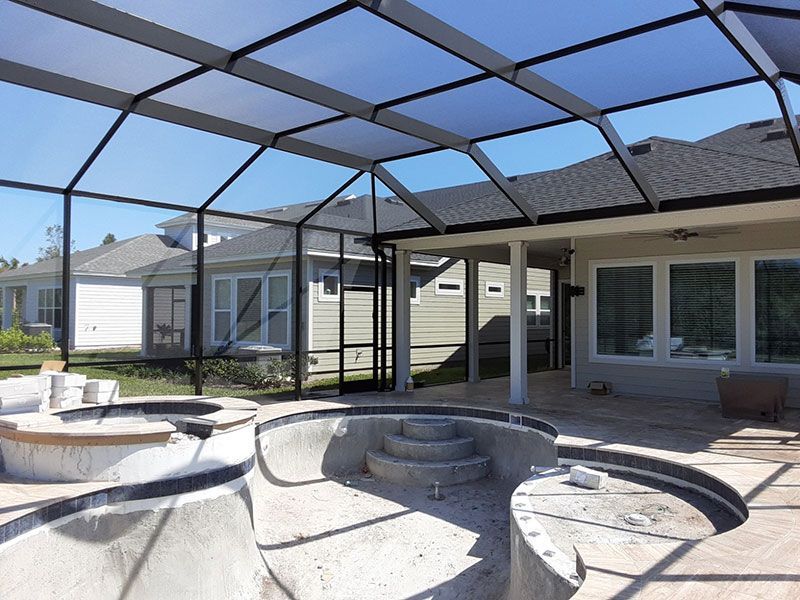 Backyard patio with screened enclosure, stone fire pit, and built-in seating under a clear roof.