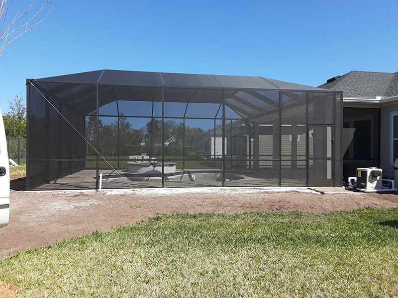 Screened backyard patio enclosure beside a house on a sunny day