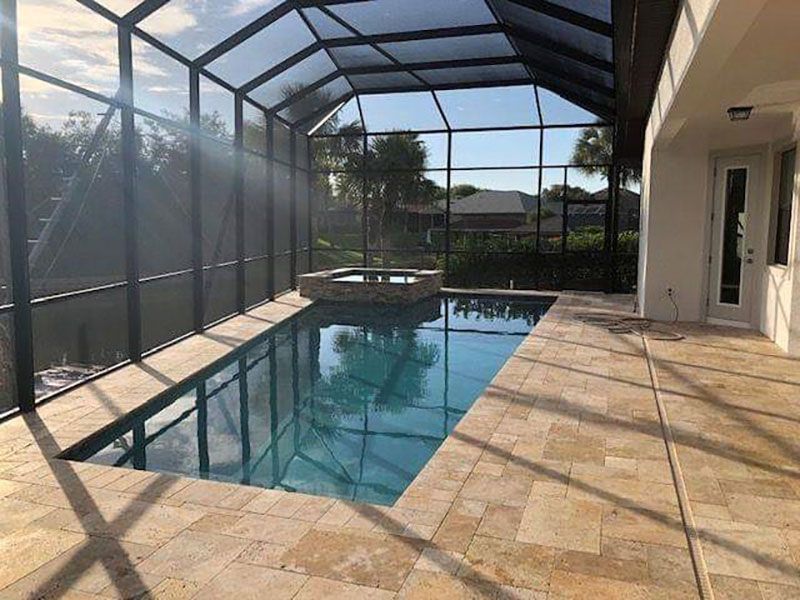 Screened-in patio with a rectangular swimming pool and tiled deck in bright sunlight