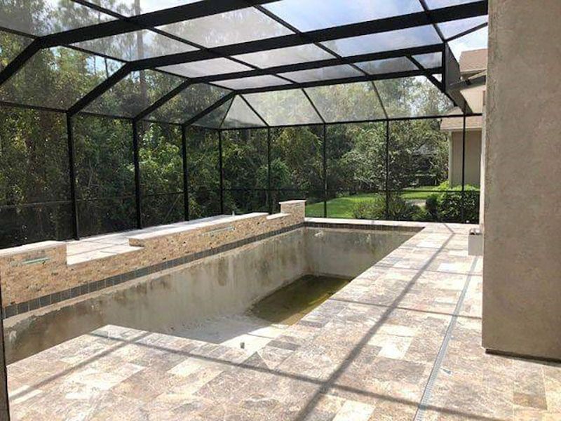 Screened-in patio with a rectangular sunken pool, stone deck, and lush greenery outside
