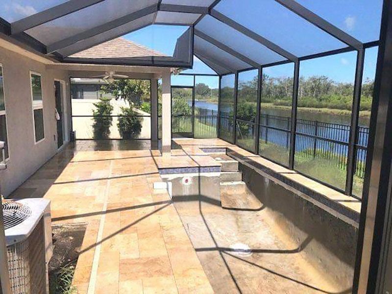 Screened patio with tan tile floor, seating, and a water view beyond the railing.